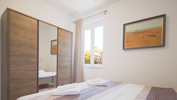 A bedroom with a bed, a wardrobe, a window, and a painting on the wall. - Apartment Goge - One-bedroom Apartment With Balcony (Dubrovnik)