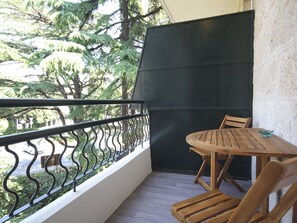 A balcony with a wooden table and chairs, a black privacy screen, and a metal railing overlooking trees. - Apartment Goge - One-bedroom Apartment With Balcony (Dubrovnik)