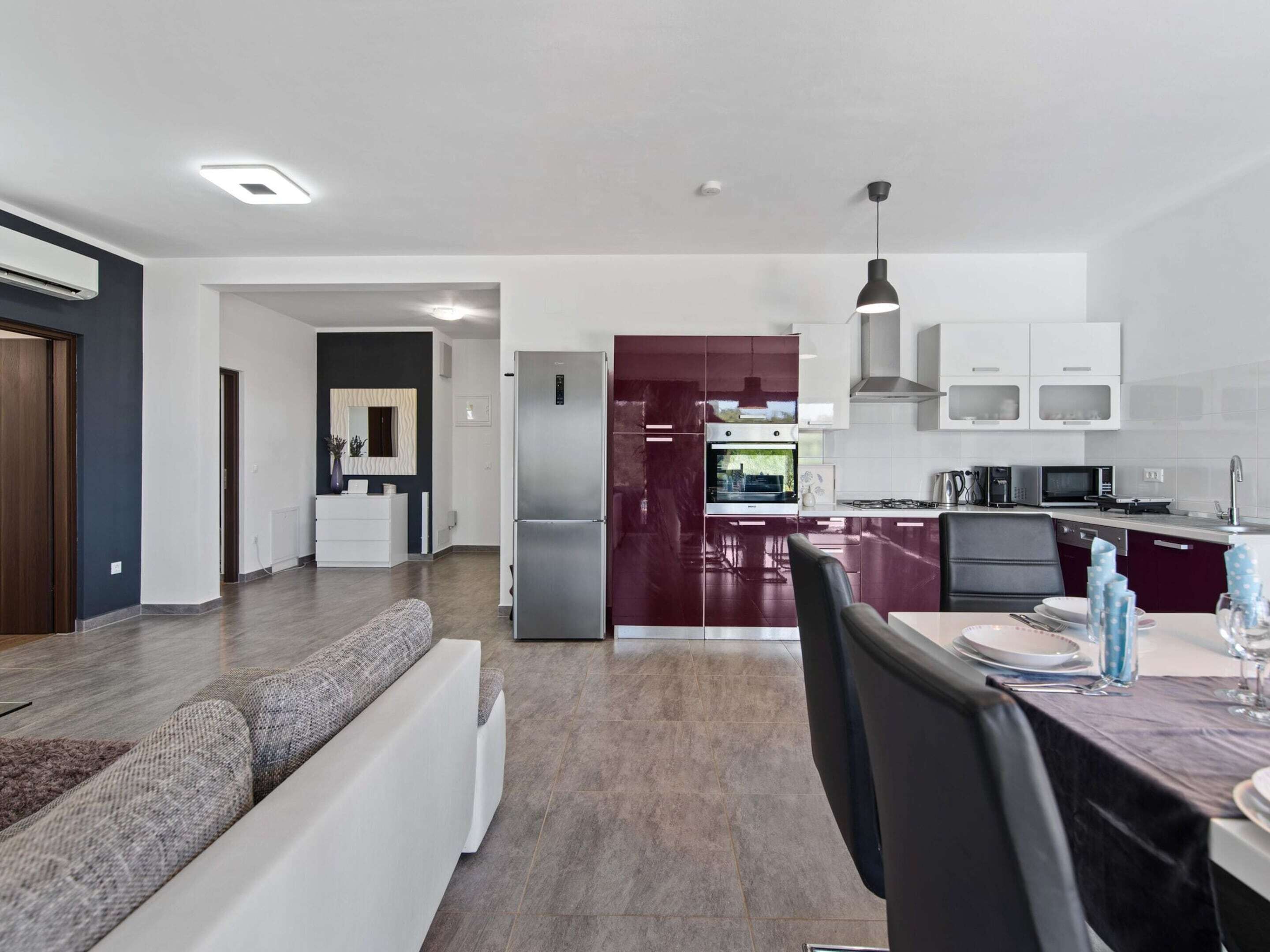 A modern kitchen with stainless steel appliances, a dining area with a table set for two, and a living room with a sofa.