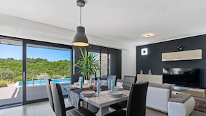 A modern dining area with a pool view, a TV, and a minimalist kitchen. - Modern Villa With Pool, Covered Terrace and sea View (Novigrad)