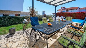 An outdoor patio with a table and chairs, a barbecue grill, and a pool in the background. - Spacious Holiday Home in Visnjan With Private Pool (Visnjan)