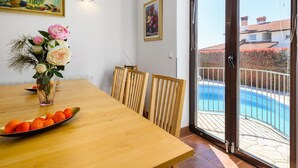 A dining area with a wooden table, chairs, a vase with flowers, and a view of a swimming pool through a glass door. - Spacious Holiday Home in Visnjan With Private Pool (Visnjan)