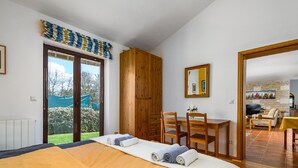 A bedroom with a bed, a wooden wardrobe, a dining table with chairs, and a view of the garden through a sliding door. - Spacious Holiday Home in Visnjan With Private Pool (Visnjan)