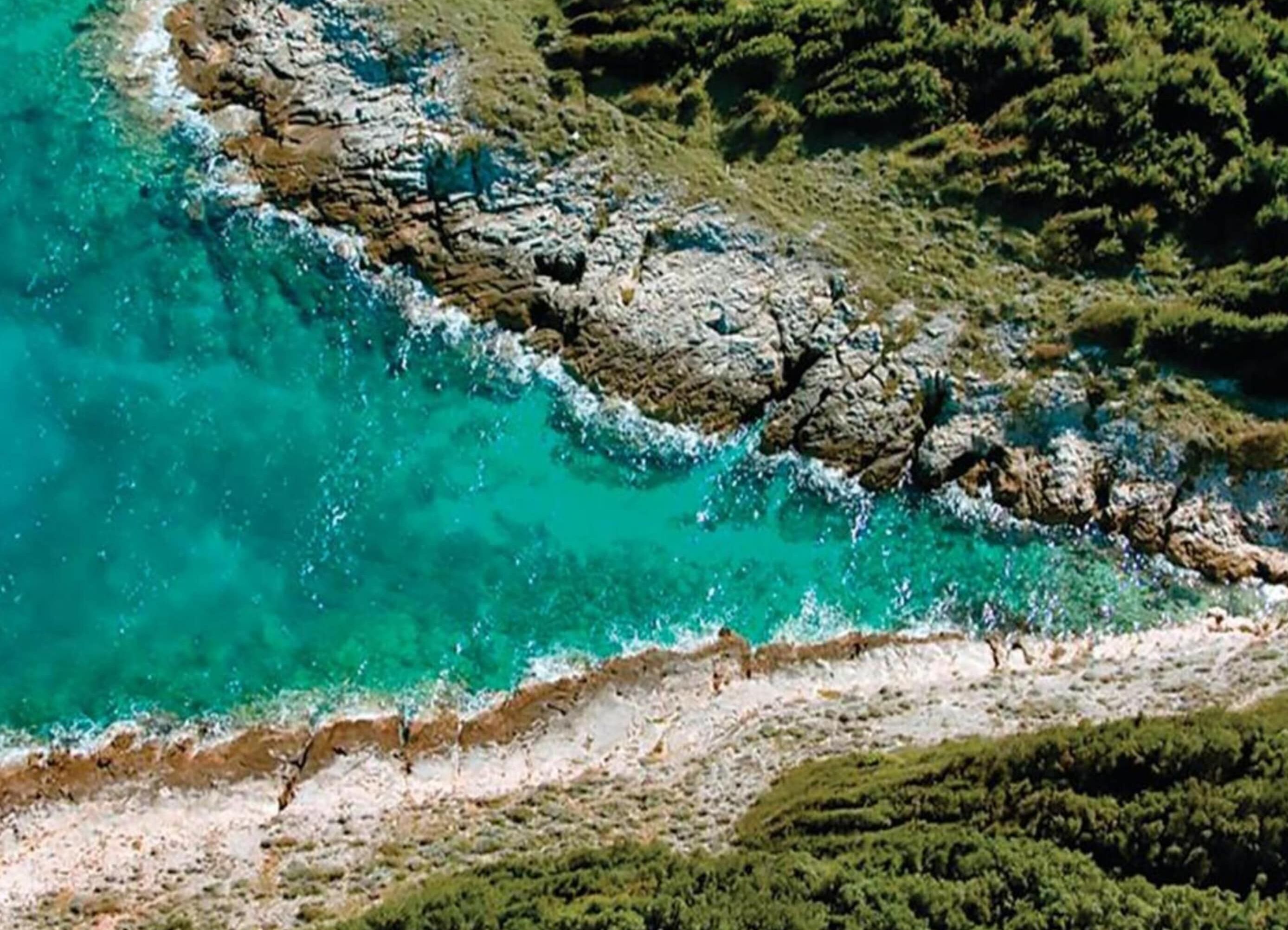 An aerial view of a coastal area with rocky terrain and clear turquoise waters.