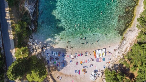 An aerial view of a beach with clear turquoise water, a sandy shore, and several beach umbrellas and sun loungers. - Apartment in Liznjan With Pool and Terrace (Liznjan)