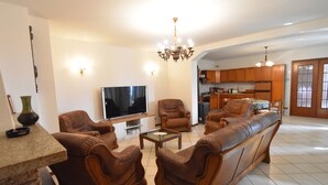 Un salon avec un canapé, des fauteuils, un téléviseur et un lustre.