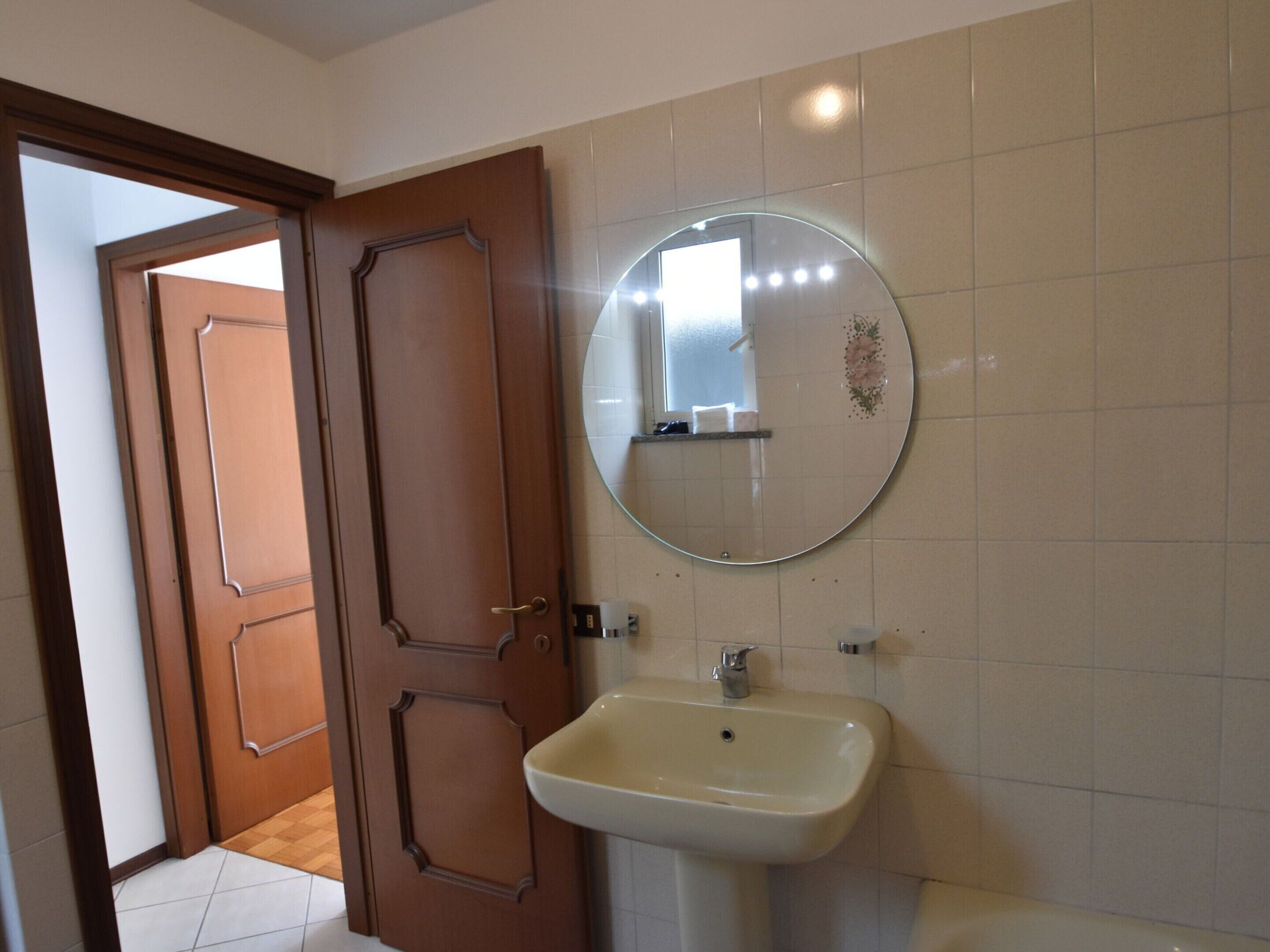 A bathroom with a white sink, a round mirror, and a wooden door.