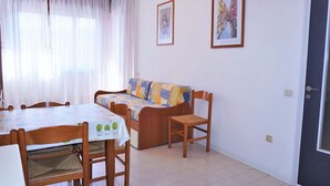 A small, well-lit room with a dining table, chairs, a sofa, and two framed pictures on the wall. - Belvilla by OYO Inviting Apartment With Pool (Caorle)