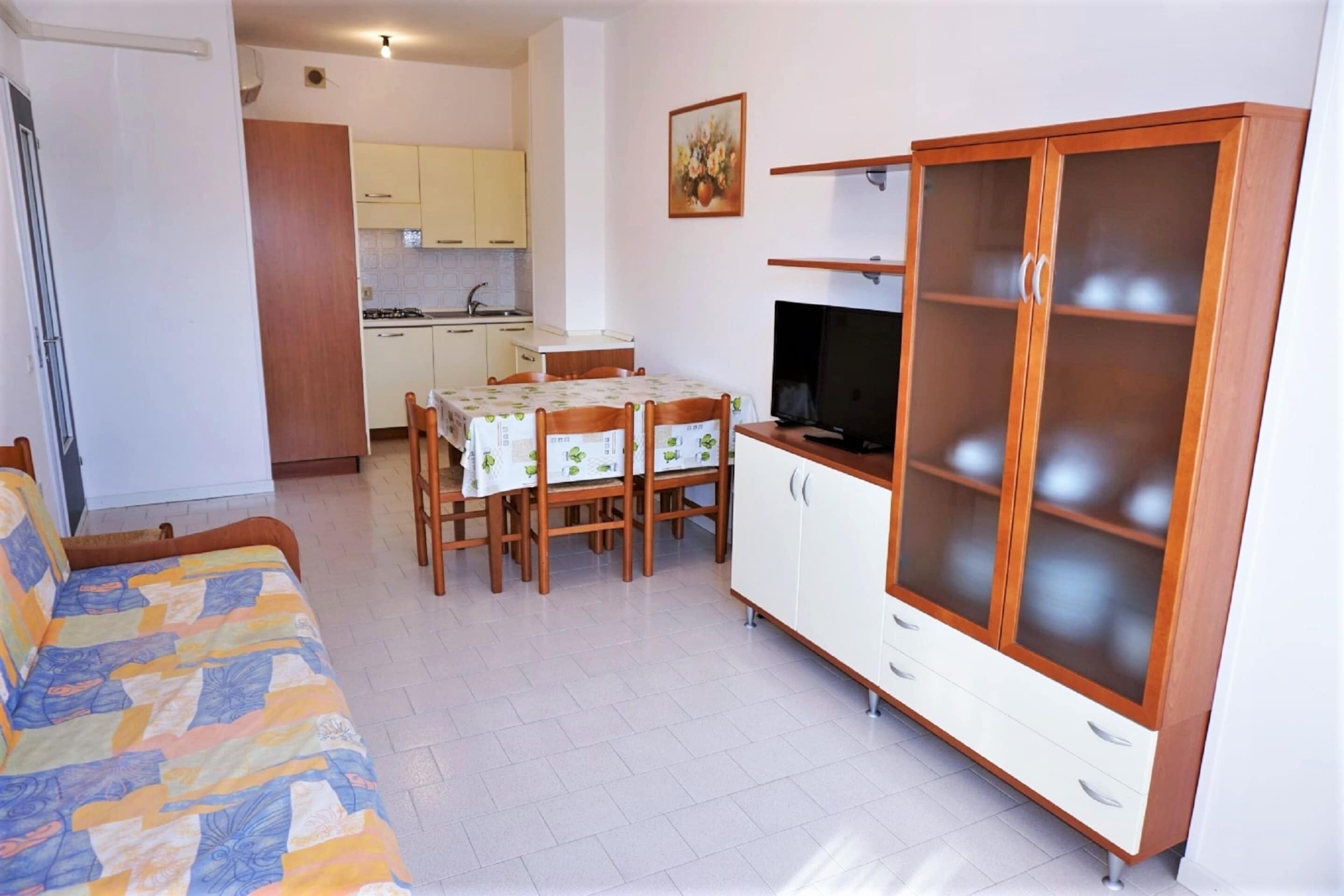 A compact living space with a sofa, a dining table with chairs, a TV, and a cabinet with glass doors.