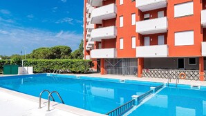 A multi-story building with balconies, a swimming pool, and a clear blue sky. - Belvilla by OYO Inviting Apartment With Pool (Caorle)