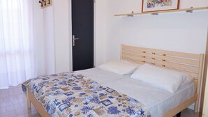 A bedroom with a bed, a door, a framed picture on the wall, and a window with curtains. - Belvilla by OYO Inviting Apartment With Pool (Caorle)
