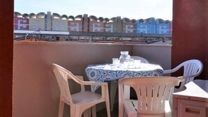 A balcony with two white plastic chairs and a small table, a patterned tablecloth, and a view of a building with a distinctive architectural design. - Belvilla by OYO Inviting Apartment With Pool (Caorle)