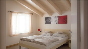 A bedroom with a bed, a nightstand, a lamp, a window with sheer curtains, and wall art. - Apartment 4 - attic second floor (Tiarno di Sopra)