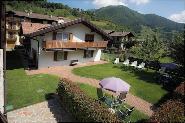 A two-story house with a balcony, a patio with outdoor furniture, and a view of a mountainous landscape.