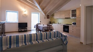 A modern kitchen with wooden cabinets, a dining area with a table and chairs, and a sofa in the foreground. - Apartment 4 - attic second floor (Tiarno di Sopra)