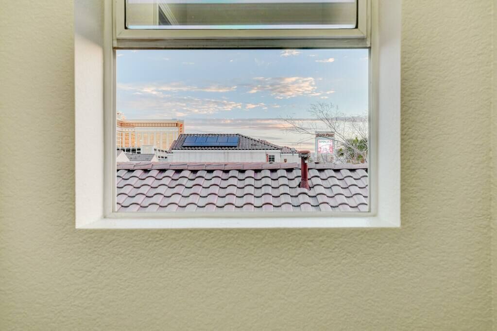 Une fenêtre donnant sur un bâtiment doté d’un toit recouvert de tuiles et d’un panneau solaire.