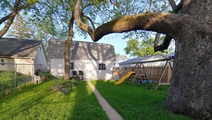 A backyard with a grassy lawn, a concrete path, a yellow slide, and a wooden play structure.
