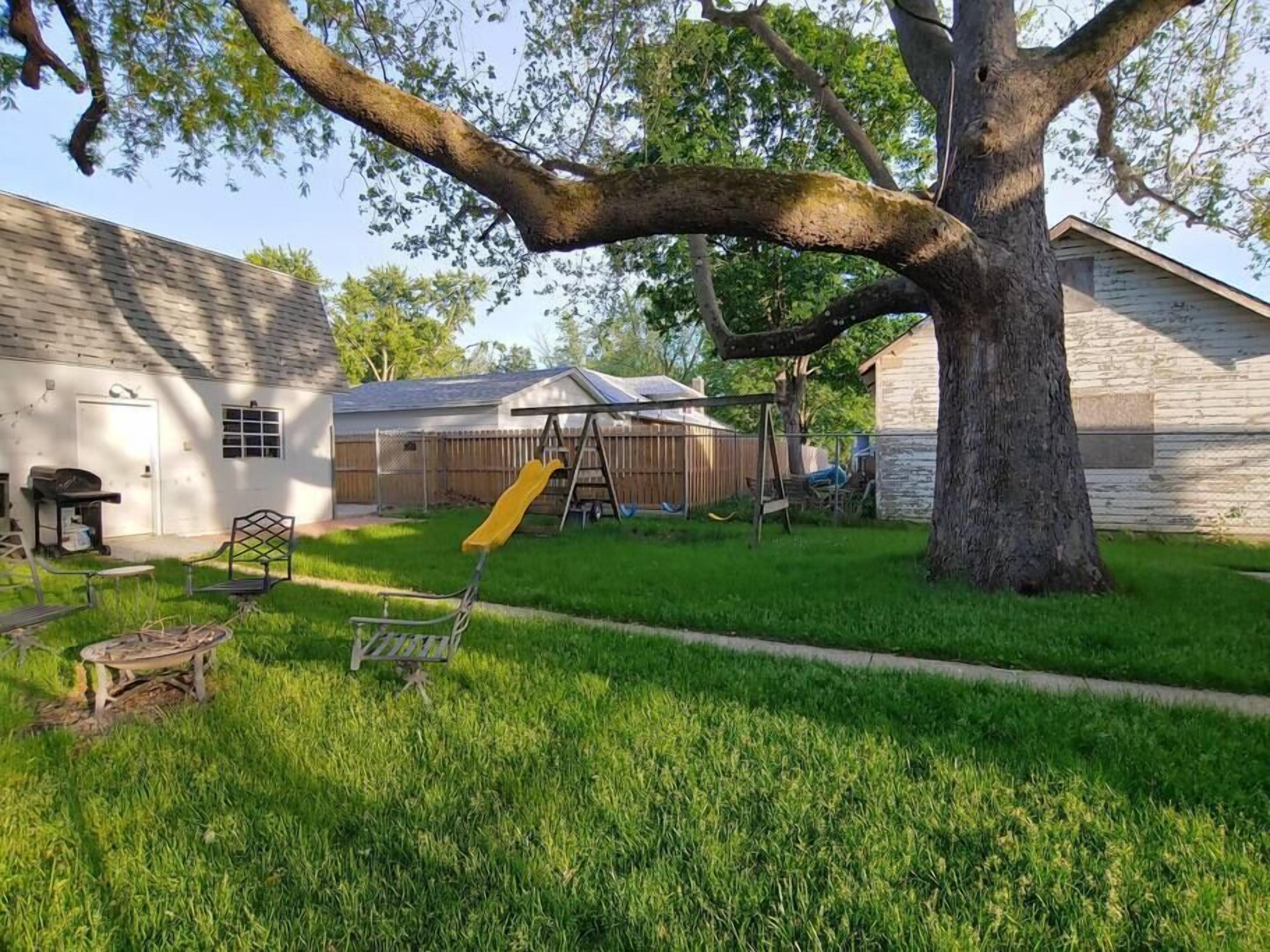 Un jardin avec une balançoire, un arbre et une maison avec un garage.