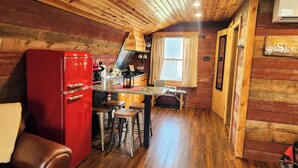 A cozy cabin-style room with a wooden ceiling, a red refrigerator, a kitchen area with a window, and a 'SLEEP' sign on the wall.