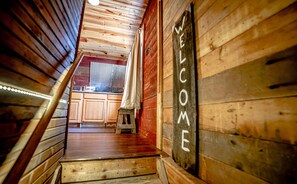 Eine Holztreppe führt zu einer Küche, in der ein 'WELCOME'-Schild hängt.