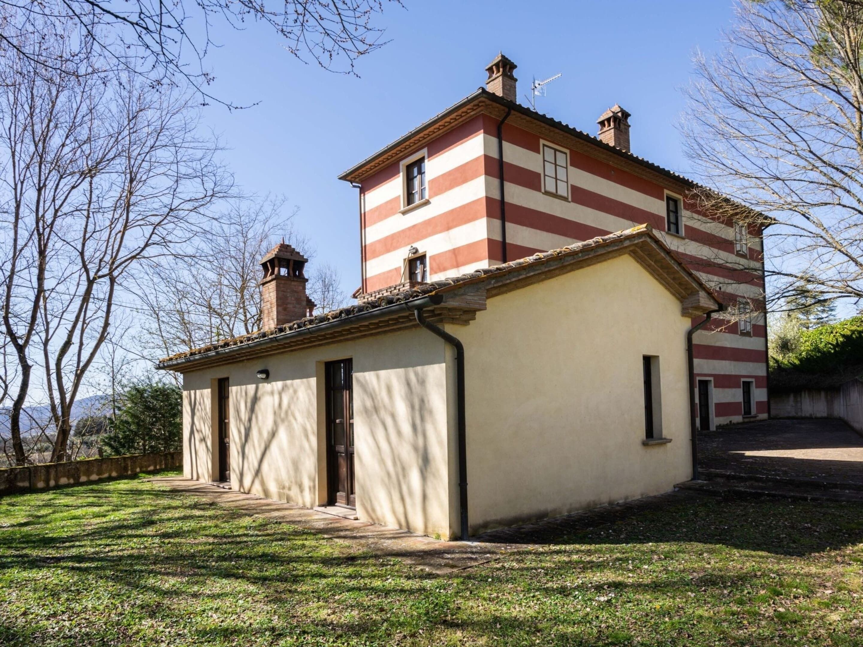 Un bâtiment à deux étages, doté d’une façade à rayures rouges et blanches, une petite construction attenante avec un toit en tuiles, et un ciel dégagé.