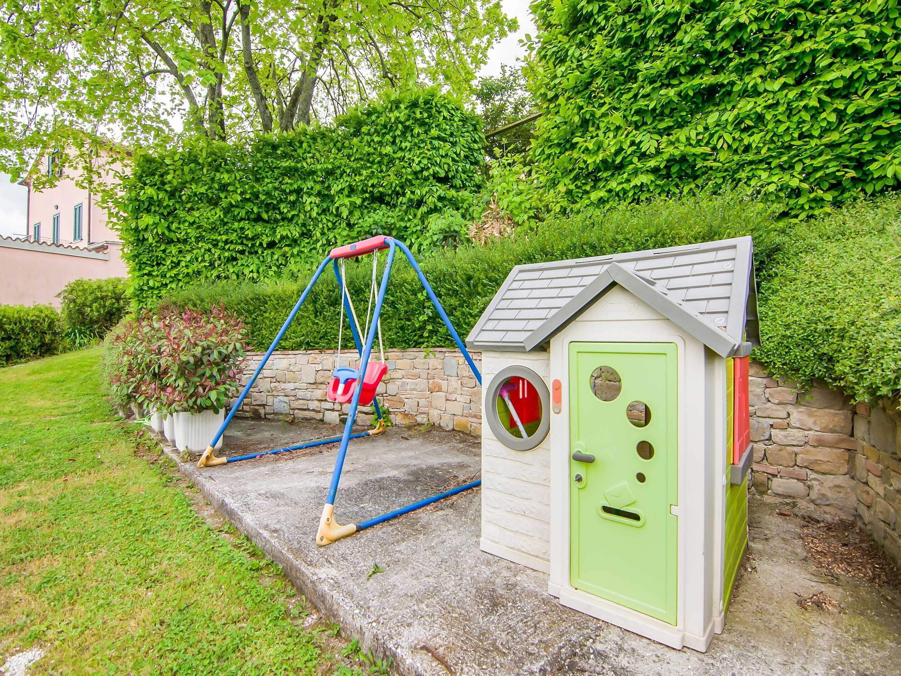 Zona infantil con un columpio y una casita de juegos con puerta y ventana.