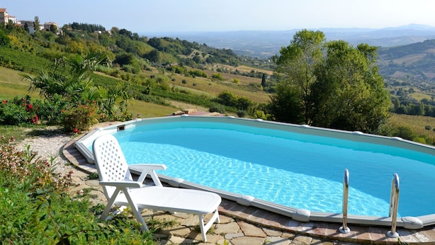 Ein Swimmingpool mit klarem, blauem Wasser, umgeben von viel Grün und Blick auf sanfte Hügel in der Ferne.