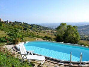 A swimming pool with clear blue water, surrounded by greenery and a view of rolling hills in the distance. - Belvilla by OYO Rose di Fratta 2 (Cupramontana)