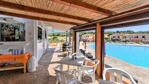 A covered outdoor area with a pool, tables, chairs, and a bar. - Belvilla by OYO Sardegna Mare 616 (Trinità d'Agultu e Vignola)