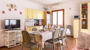 A compact living space with a dining area, kitchen, and a TV. - Belvilla by OYO Sardegna Mare 616 (Trinità d'Agultu e Vignola)