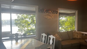 A dining area with a table and chairs, a sofa, and a rug. There is a sign on the wall that reads "Lake House."