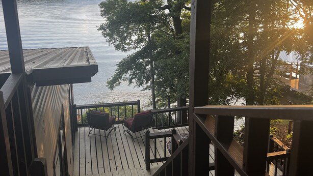A wooden deck with a railing overlooking a body of water, surrounded by trees.