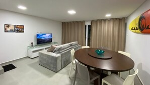 Una sala de estar moderna con un sofá, un televisor, una mesa de comedor con sillas y una tabla de surf en la pared.