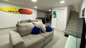 Una sala moderna con un sofá color beige, una decoración con una tabla de surf, una mesa de comedor y una escalera.