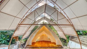Une structure en forme de tente, dotée d’une plateforme centrale en bois et d’une armature métallique.