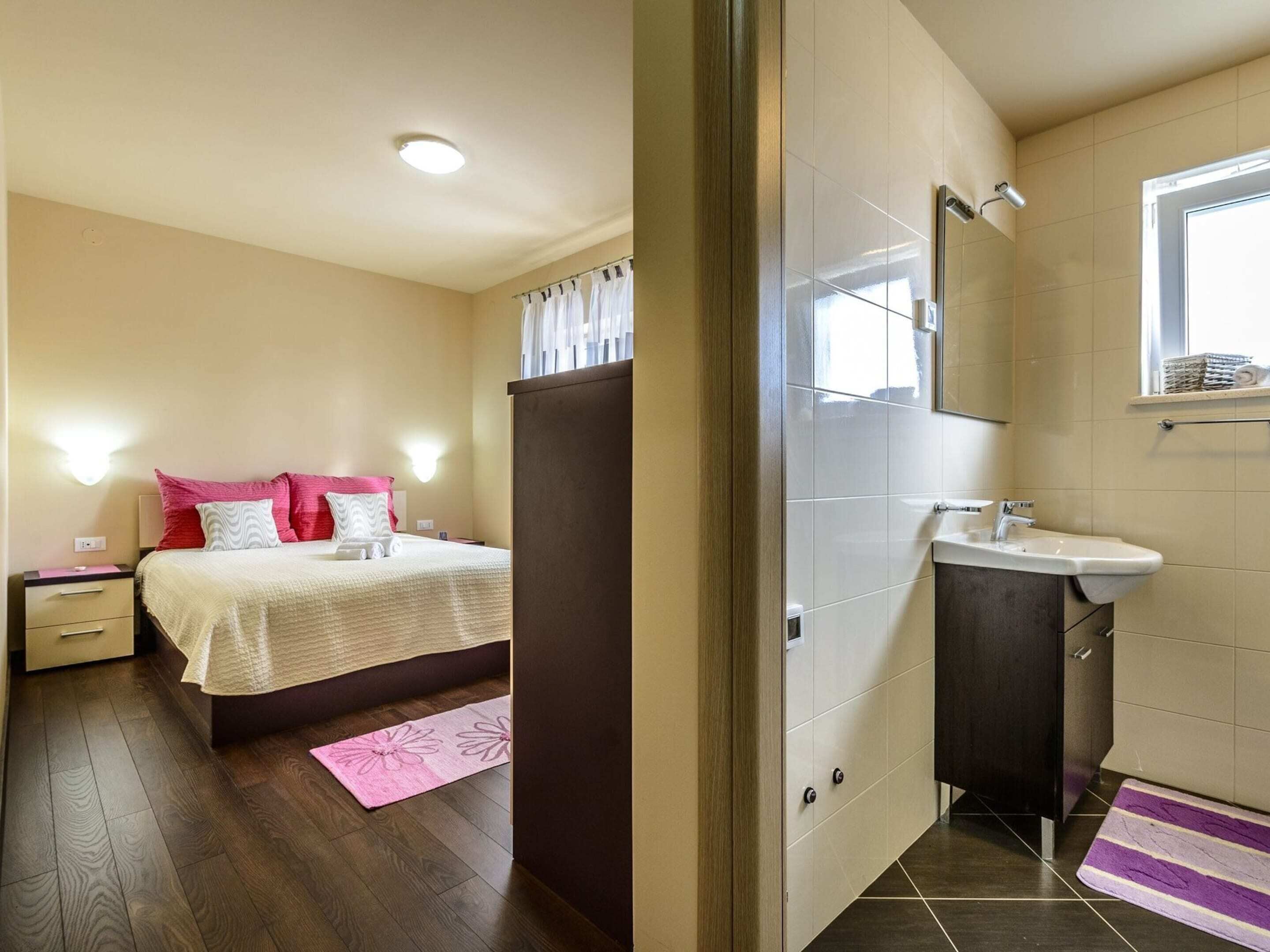Ein Schlafzimmer mit Bett, Nachttisch und einem Badezimmer mit Waschbecken und Spiegel.