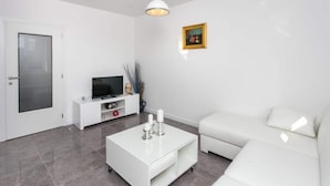 Ein modernes Wohnzimmer mit einem weißen Sofa, einem Couchtisch, einem Fernseher auf einem weißen Schrank und einem Gemälde an der Wand.