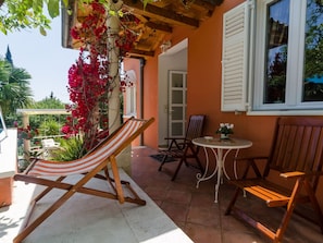 A patio with a striped hammock, a round table, and two wooden chairs.