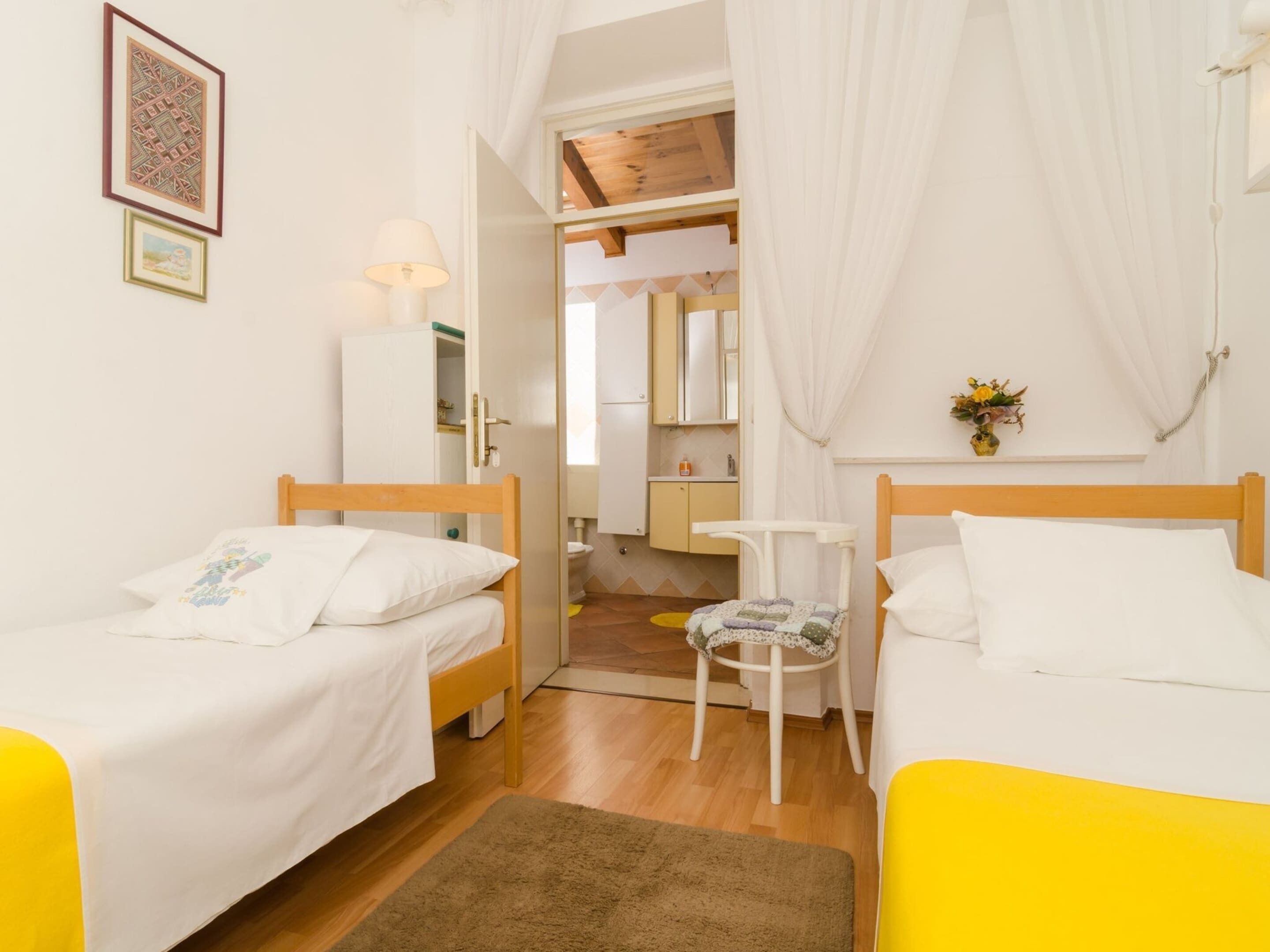 Une chambre avec deux lits, une petite table, une chaise, une lampe, un miroir et une porte donnant sur une salle de bain.