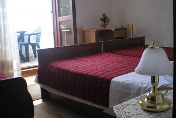 Un dormitorio con dos camas, una mesita de noche con lámpara, una silla y una ventana que ofrece vistas a muebles de exterior.