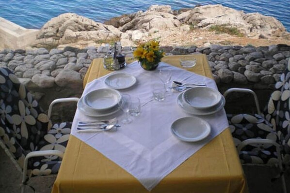 A table set for four with a white tablecloth, plates, cutlery, and a vase of yellow flowers.