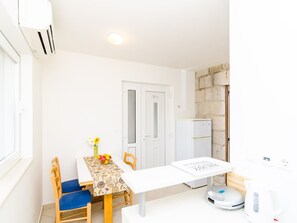 A small, bright kitchen with a white table, chairs, a refrigerator, and a kettle. - Apartments Nikola - One Bedroom Apartment With Terrace and Garden View (Dubrovnik)