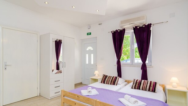 A bedroom with a wooden bed, two bedside tables, a wardrobe, and a window with purple curtains.