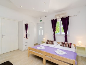 A bedroom with a wooden bed, two bedside tables, a wardrobe, and a window with purple curtains.