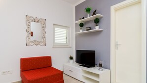 A room with a red sofa, a TV on a white stand, a mirror, and shelves with plants.