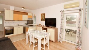 A modern kitchen with white cabinets, a dining table with chairs, a flat-screen TV, and a large window with curtains. - Green Hills Apartment - One Bedroom Apartment With Balcony and Sea View (Dubrovnik)