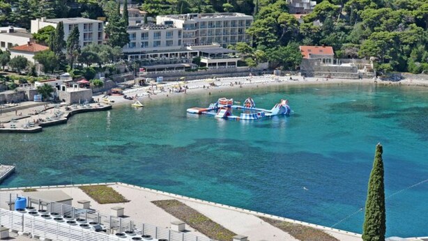 A coastal town with a clear blue sea, a pier with boats, and buildings along the shore. - Green Hills Apartment - One Bedroom Apartment With Balcony and Sea View (Dubrovnik)