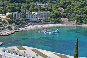 A coastal town with a clear blue sea, a pier with boats, and buildings along the shore. - Green Hills Apartment - One Bedroom Apartment With Balcony and Sea View (Dubrovnik)