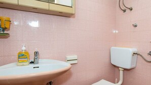 Ein Badezimmer mit einer rosa gefliesten Wand, einer weißen Toilette und einem Waschbecken mit einer gelben Handseifenflasche.