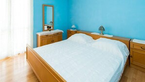 Ein Schlafzimmer mit einem Bett, Nachttischen aus Holz, einem Spiegel und einem Fenster mit Vorhängen.